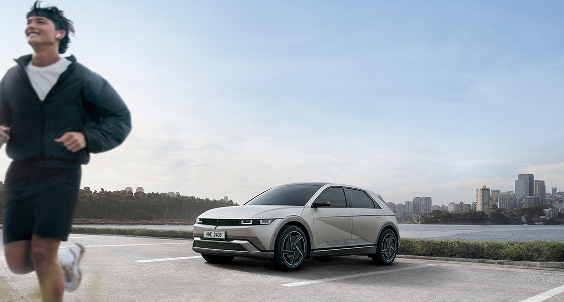 A man running in front of a car parked by the river