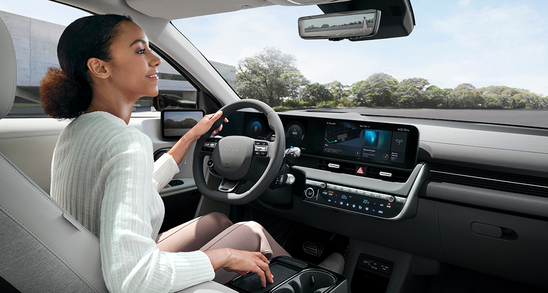 The woman is looking in the rearview mirror while holding the steering wheel