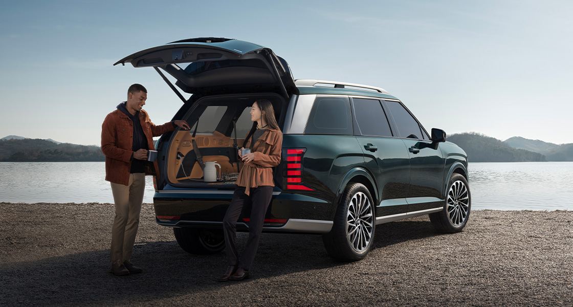 A man and a woman standing by the open tailgate of the all-new PALISADE