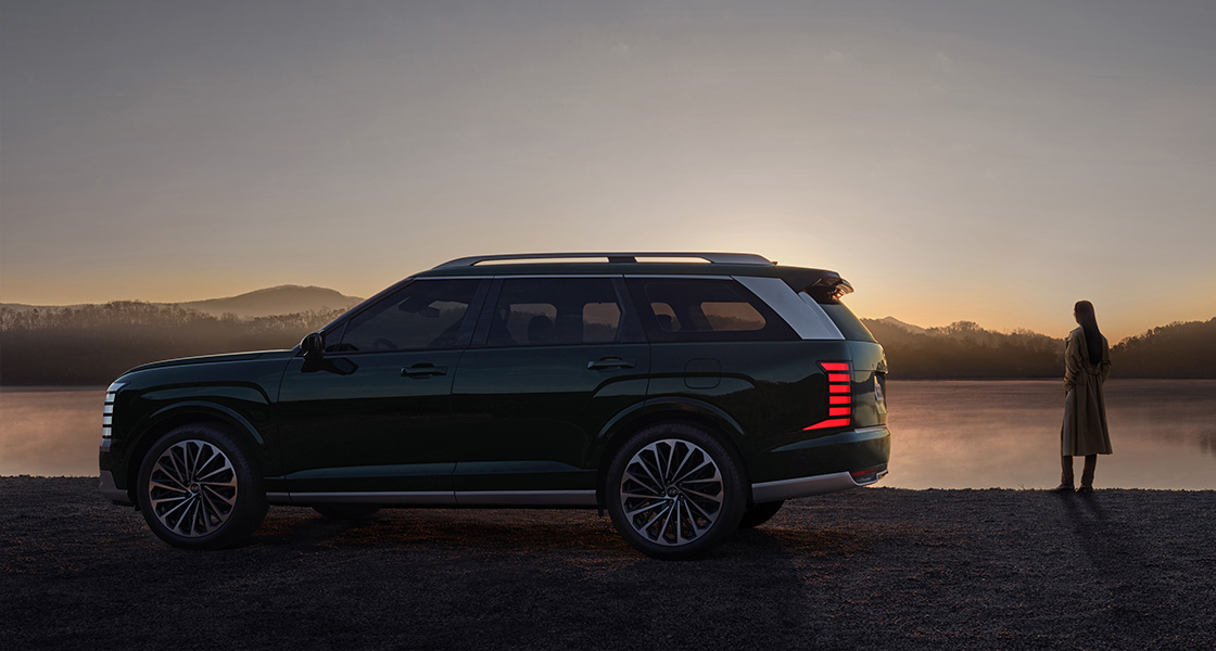The all-new PALISADE side view, and a woman standing near the vehicle.