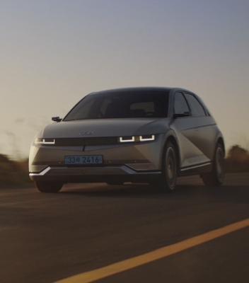 A silver IONIQ 5 driving along a highway at dusk with its white parametric pixel headlights on.