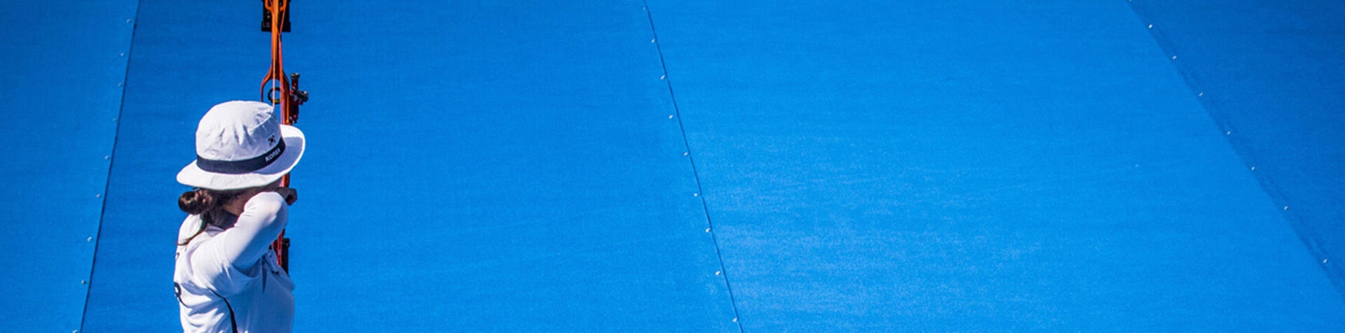 A female Korean archery team member draws her bow and focuses.