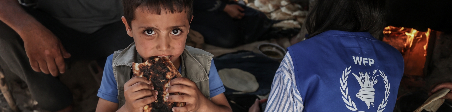 A boy in a refugee camp eats a piece of bread