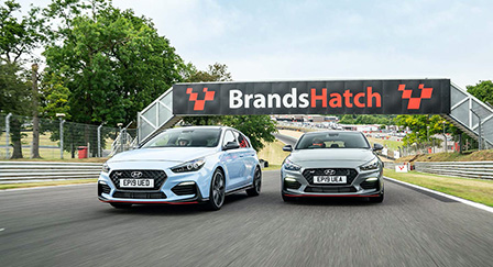 Two Hyundai N cars lined up at a starting line at the Brands Hatch racetrack.