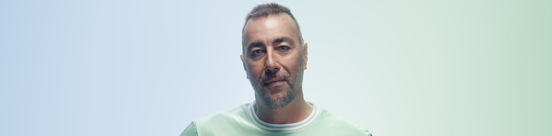 Portrait of world-renowned sculptor and new Team Century member Lorenzo Quinn smiling into the camera in front of a blue and green background.