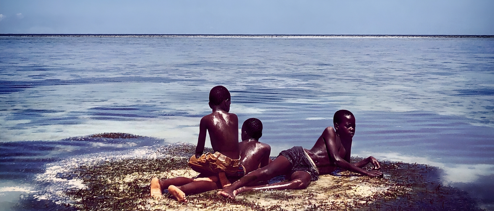 Three boys sitting on the last remaining piece of land surrounded by ocean. 